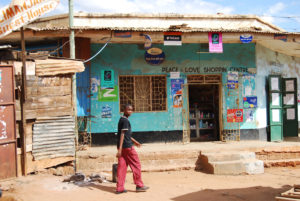 Small shop with a blue-painted exterior, wall posters, and a person walking past, photographed at the Kenya–Tanzania border.