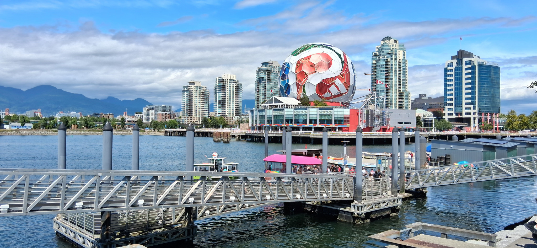 Waterfront view of Vancouver, British Columbia, featuring Science World’s geodesic dome, modern skyline, small boats, and mountains under a bright blue sky in a host city for the FIFA World Cup 2026.